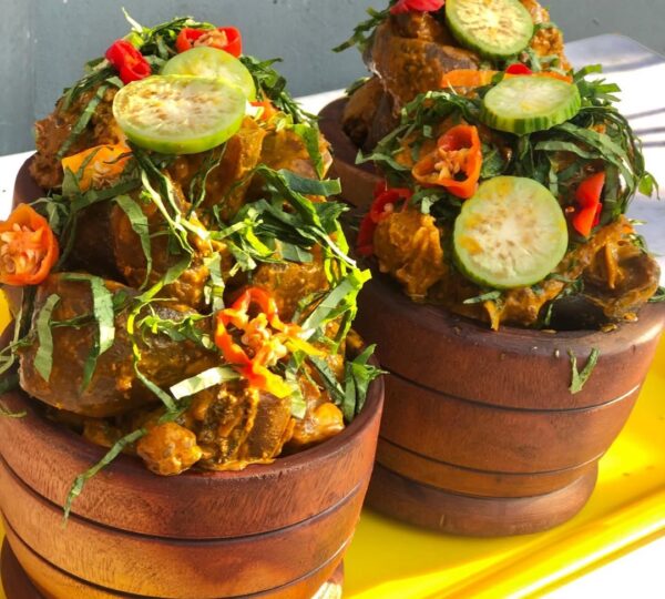 A bowl of spicy Nkwobi cow foot delicacy in palm oil sauce, symbolizing the indulgent nightlife side of Lagos street food.