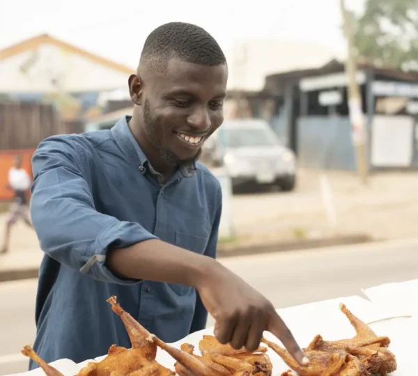 Man smiling while grilling Nigerian suya at a roadside stand in Lagos, capturing the authentic street food experience.