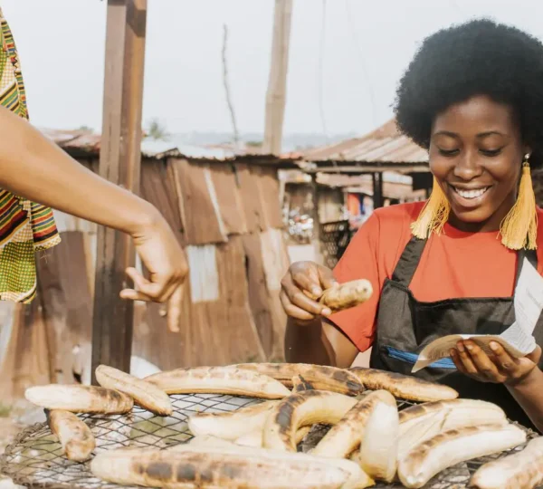 A cheerful vendor grilling ripe plantains over charcoal at a Lagos street food stall, creating the signature smoky boli aroma.