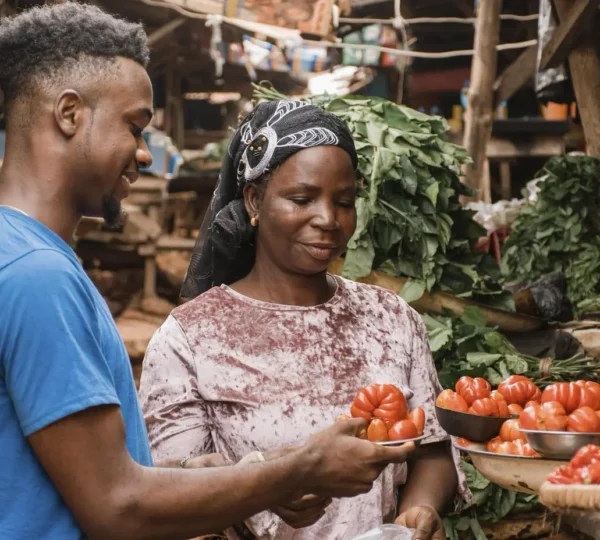 A shopper and market vendor smiling while buying fresh tomatoes at a local market in Lagos, Nigeria.