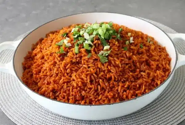 A bowl of healthy Nigerian food featuring jollof rice garnished with fresh vegetables.