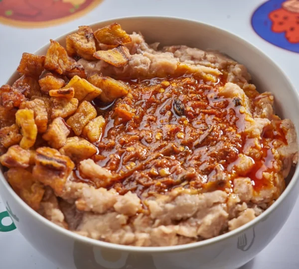 Ewa Agoyin topped with spicy sauce and crispy plantain — a favorite comfort meal on the Naija Food Tour.