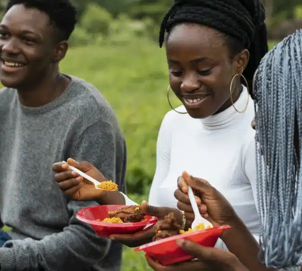 Young Nigerians sharing a local meal outdoors, enjoying authentic flavours on a food tour in Lagos Nigeria.